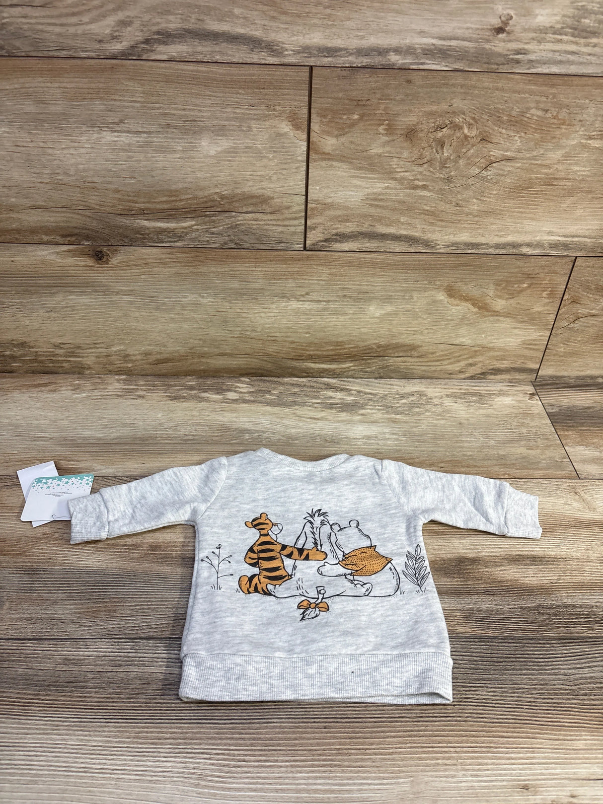 Back view of newborn grey Disney pullover sweatshirt with Winnie the Pooh and Tigger print, ribbed hem on wood background