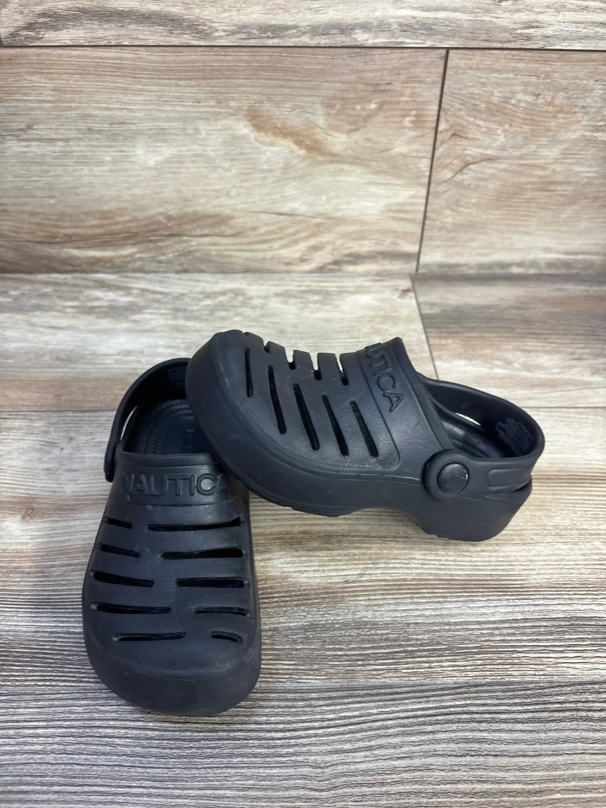 Angled view of black Nautica clogs showcasing ventilation slits, heel strap and molded logo on wood floor