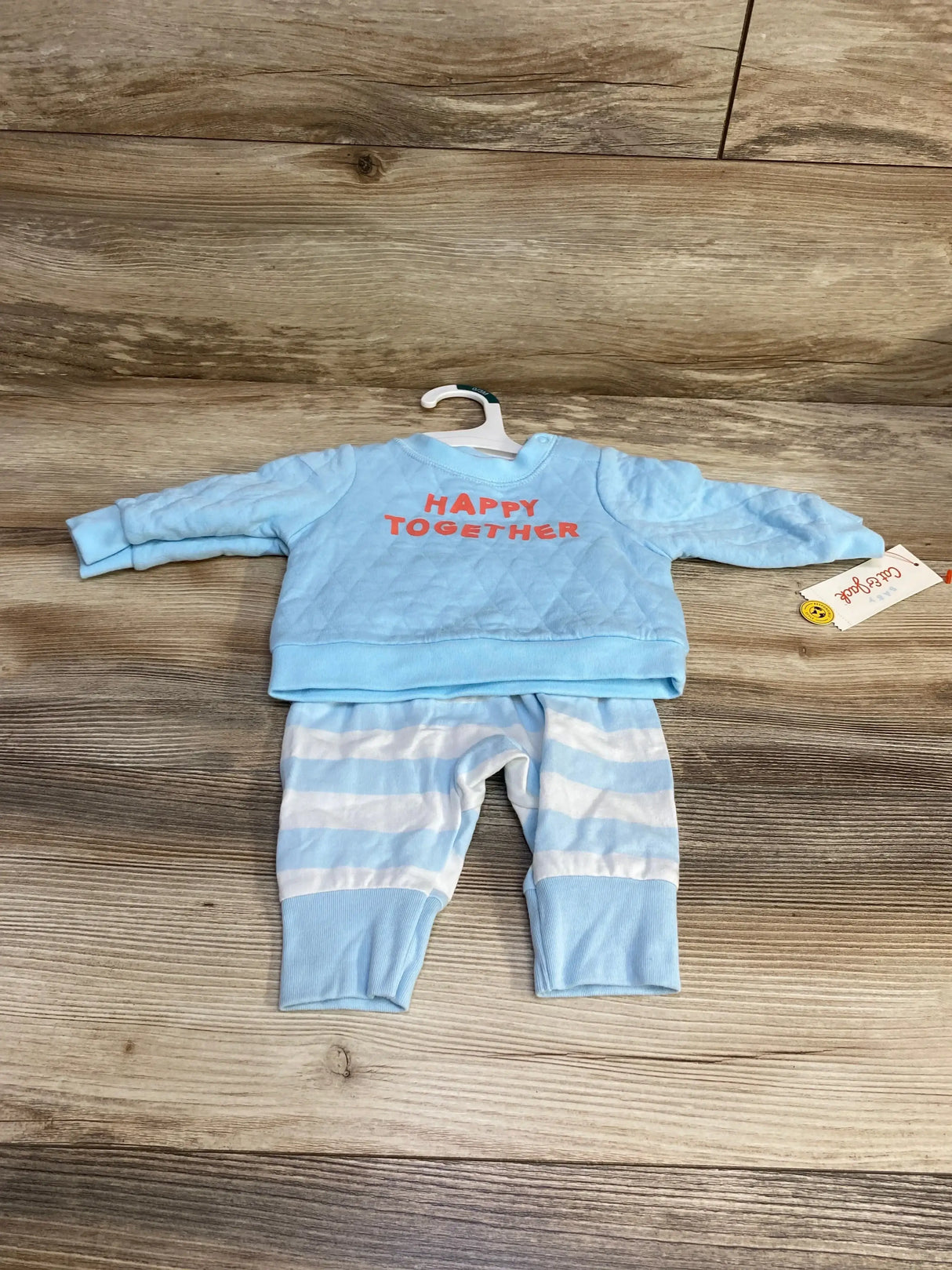 Flat lay of Cat and Jack newborn blue 2-piece sweatshirt and pants showing 'Happy Together' chest lettering and blue-white striped pants on wood background