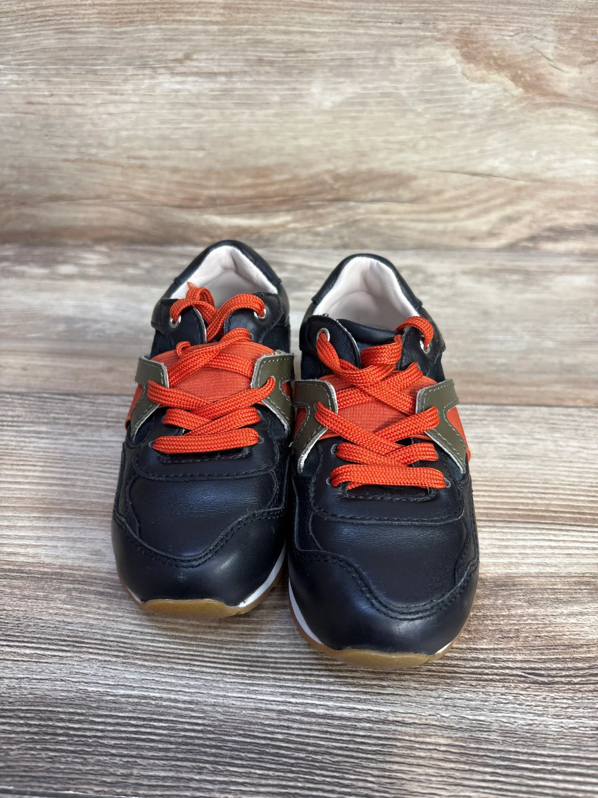 Dolce & Gabbana Bambino black leather sneakers with orange laces on a wooden surface