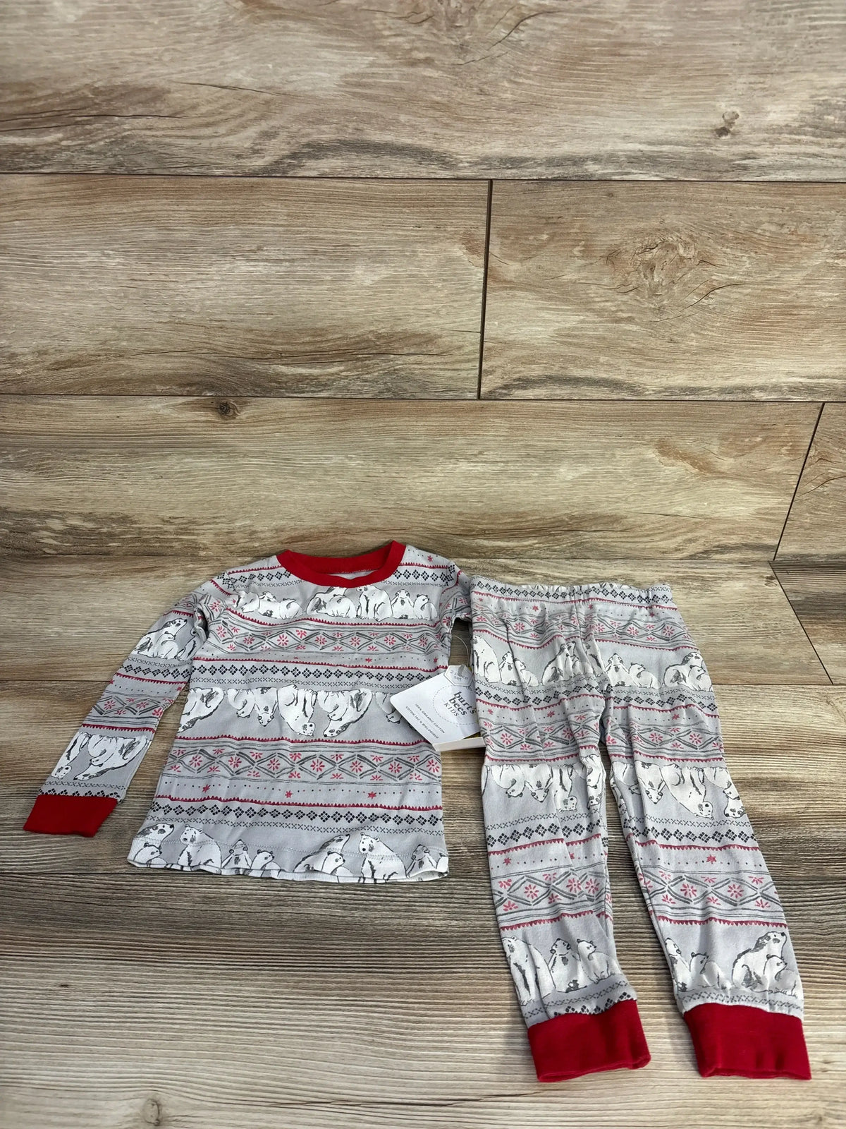 Children's two-piece pajama set with polar bear and snowflake pattern, red cuffs and collar on wood floor