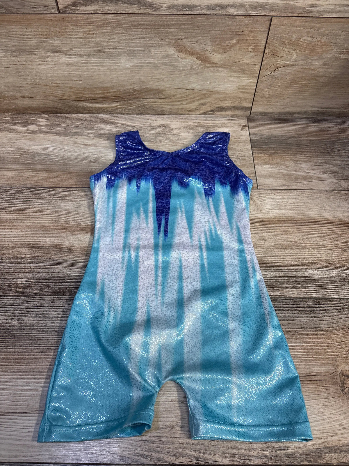 Top-down view of toddler gymnastics unitard size 2-3T with navy-to-teal ombre, white vertical streaks and metallic shimmer on wood floor