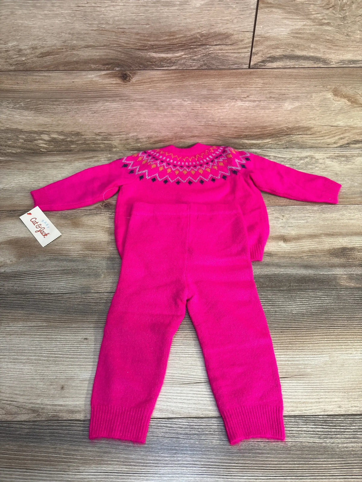 Flat lay of Cat & Jack 2-piece Fair Isle sweater and pants in hot pink showing patterned yoke and ribbed cuffs on wood floor