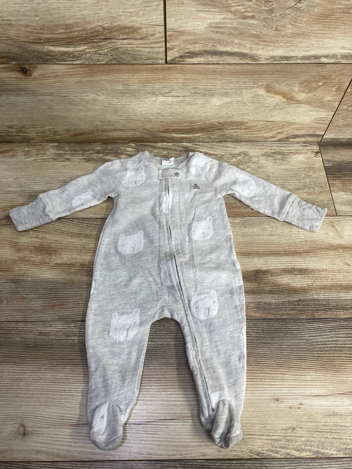 Light gray baby onesie with white bear patches, full-length zipper, against wooden floor