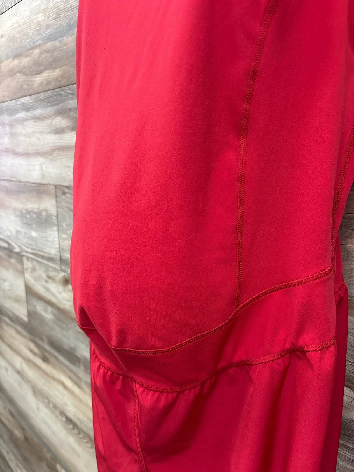 Close-up side view of Isabel maternity active romper showing red fabric, ruched belly panel and seams on wood background