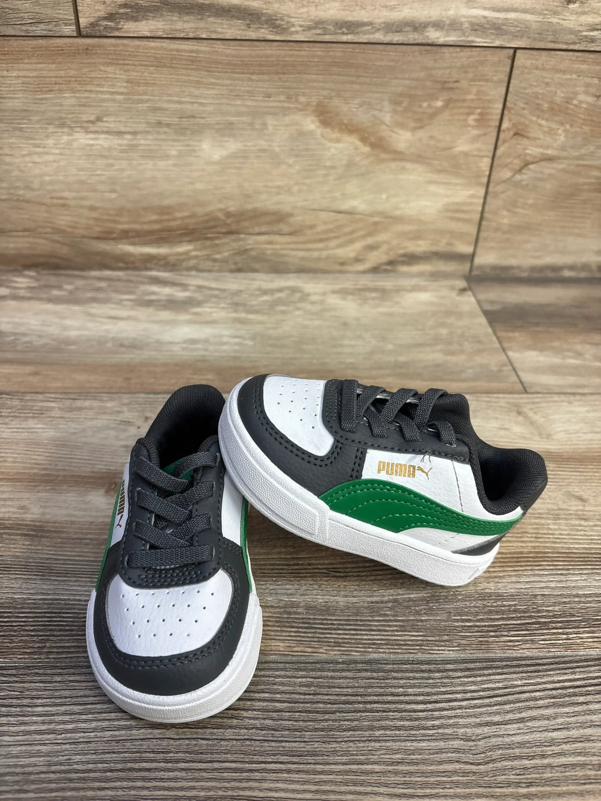 Angled view of Puma Caven 2.0 sneaker in white, black and green showing perforated toe and green side stripe on wood floor