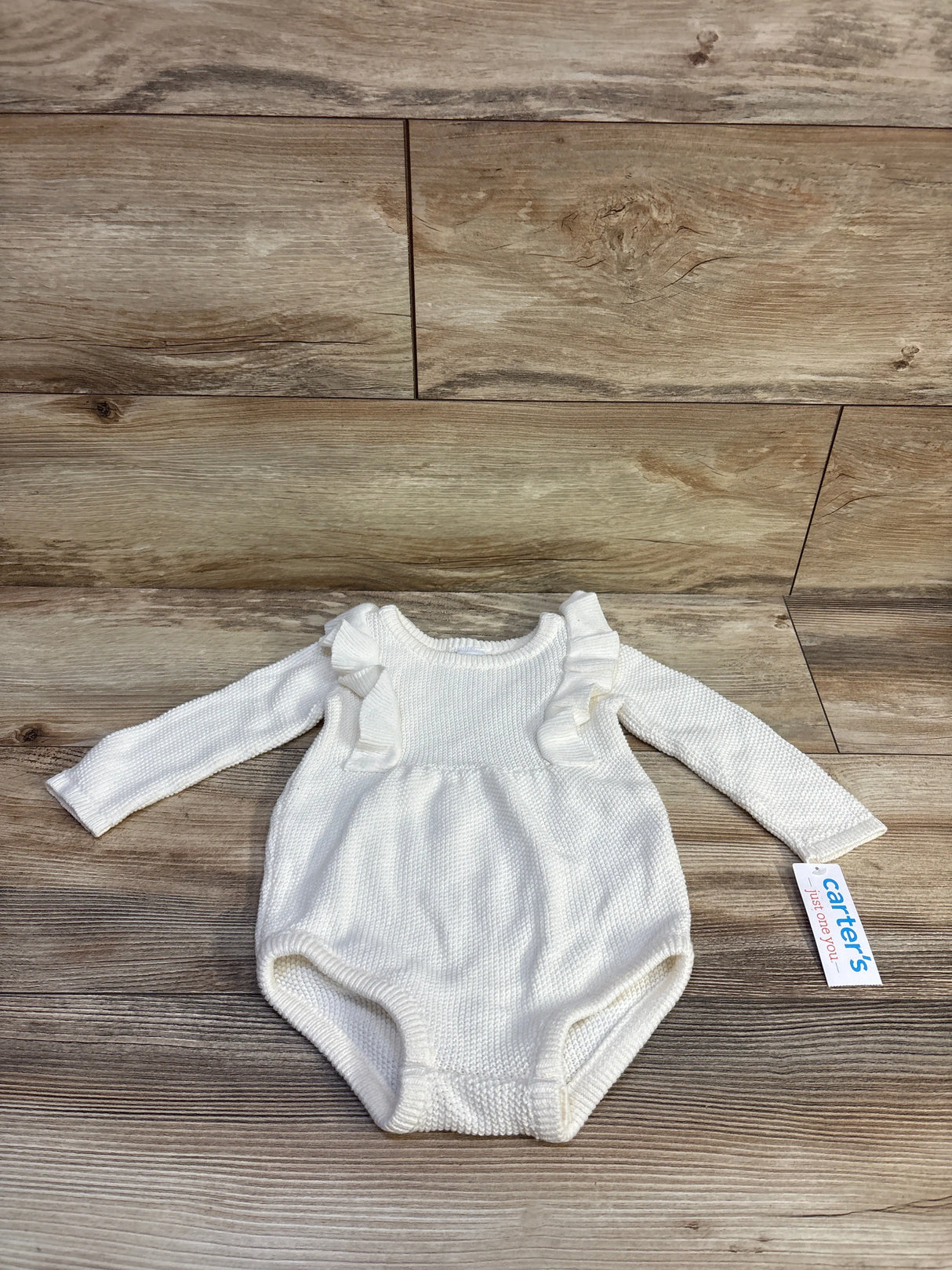 Flat lay of white knit bubble romper showcasing ruffled shoulders and long sleeves on wood plank background