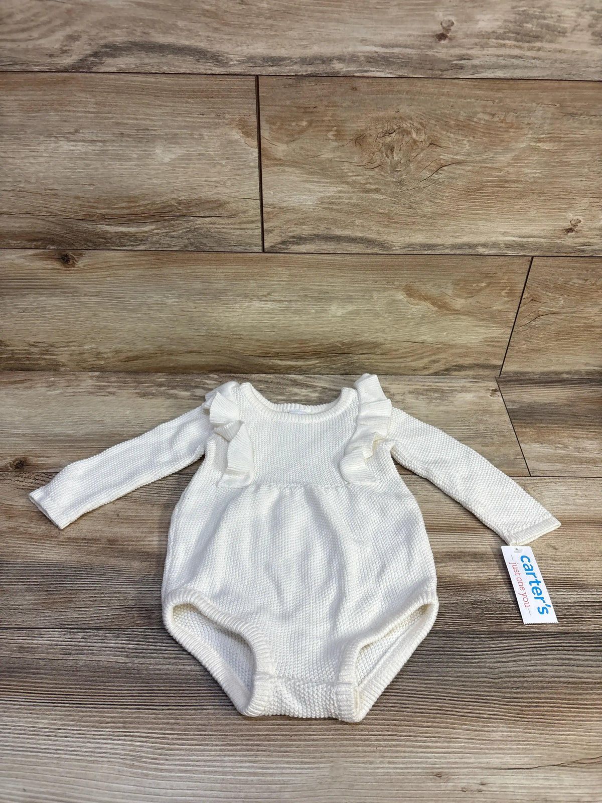 Flat lay of white knit bubble romper showcasing ruffled shoulders and long sleeves on wood plank background