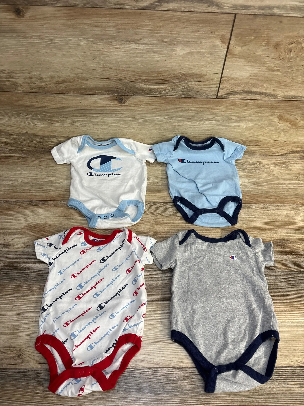 Champion baby onesies in white, blue, gray, and multi-color print on wood floor