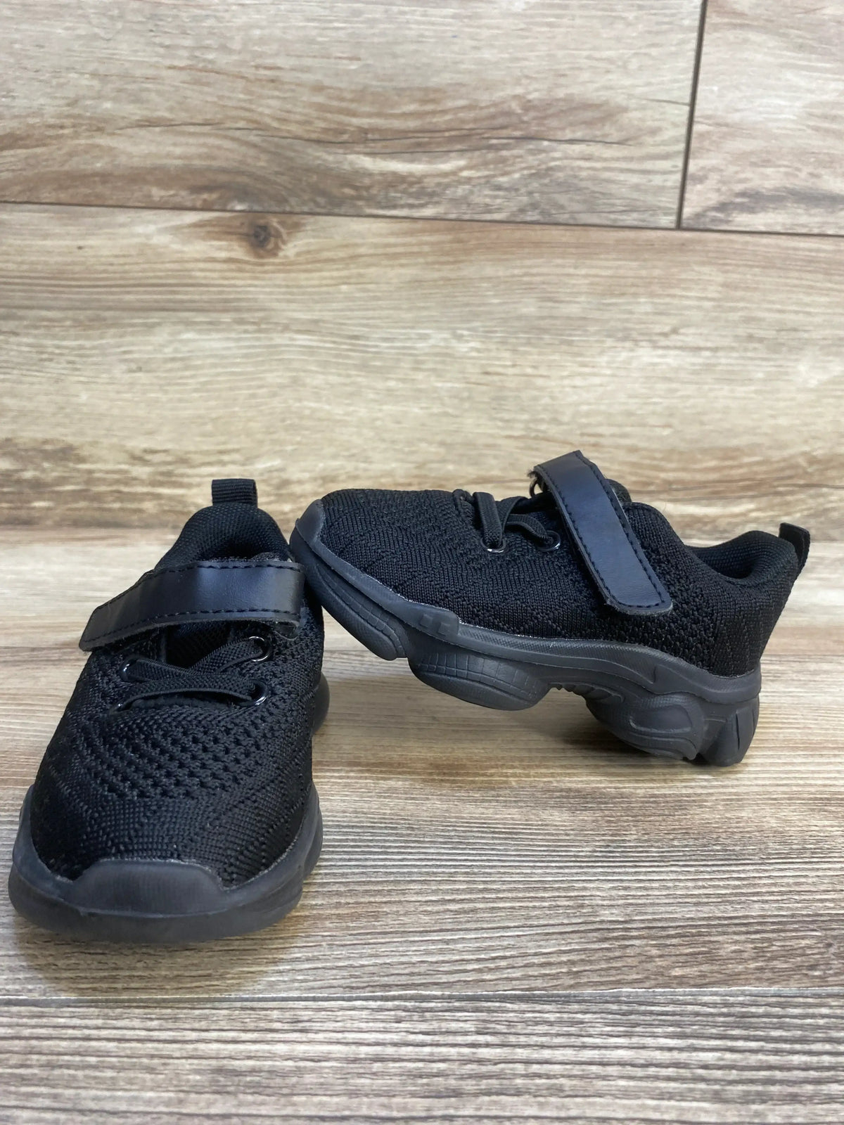 Black toddler sneakers with Velcro straps and mesh fabric on wooden floor