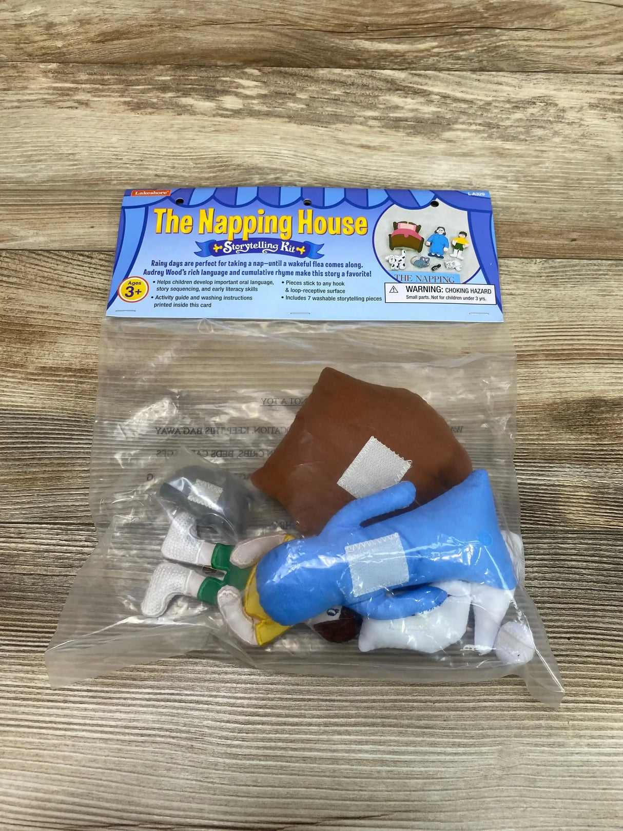 Top-down view of The Napping House storytelling kit in sealed clear bag showing plush story characters and header card on wood background