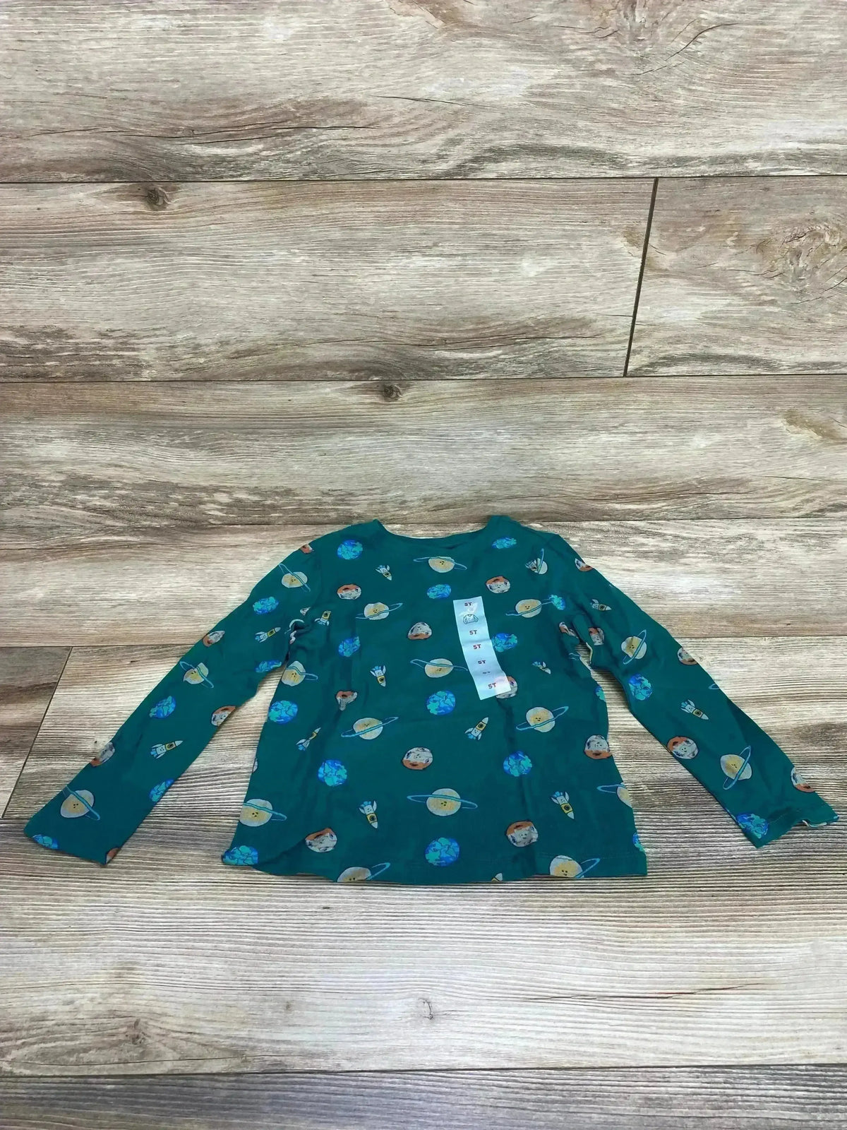 Flat lay of Old Navy green long-sleeve toddler shirt showing planet and rocket print on wood floor background