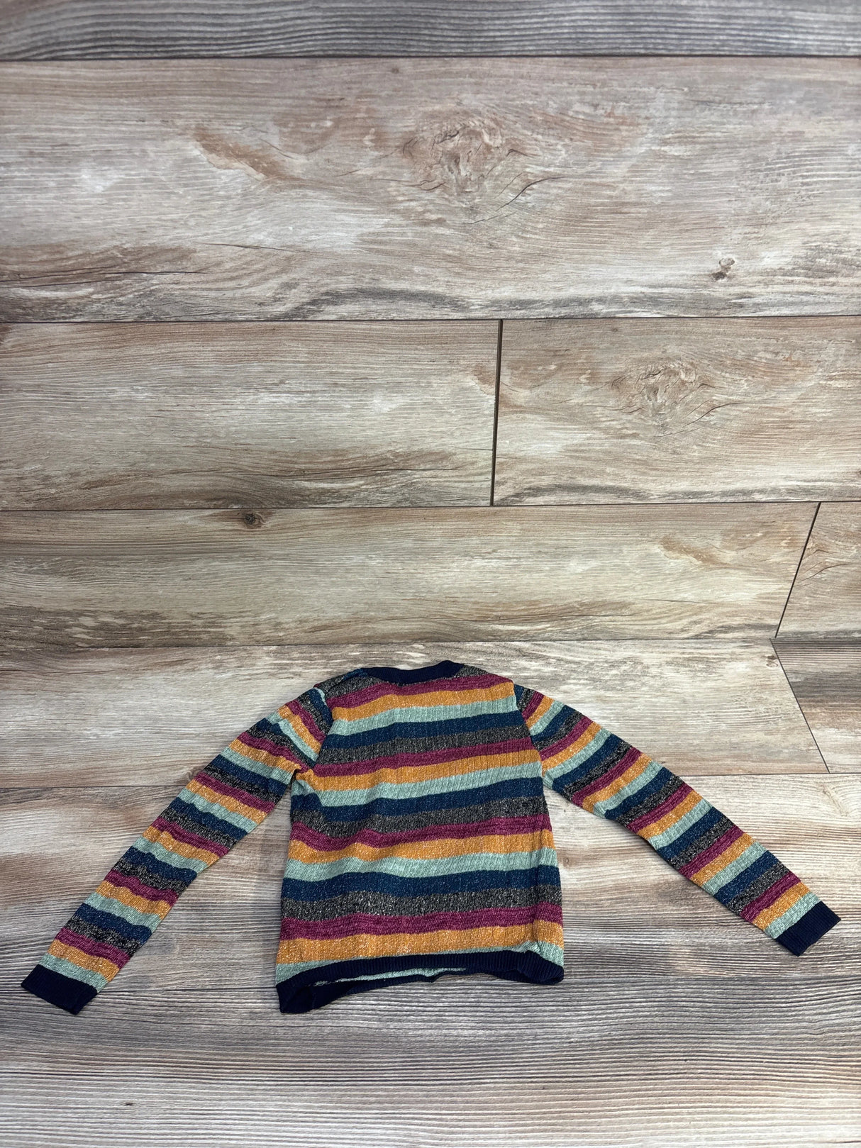 Back view of 4T Scotch & Soda pullover with metallic multicolor horizontal stripes and navy ribbed cuffs on wood floor