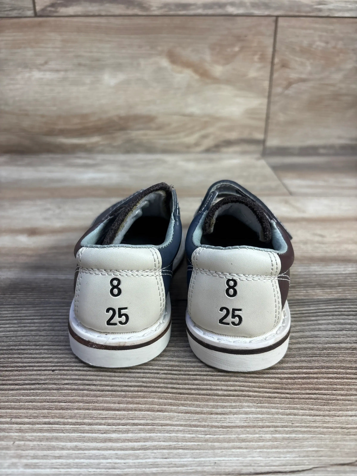 Rear view of Brunswick bowling sneakers in brown, size 8C, showcasing heel markings 8 and 25 on a wood-look floor