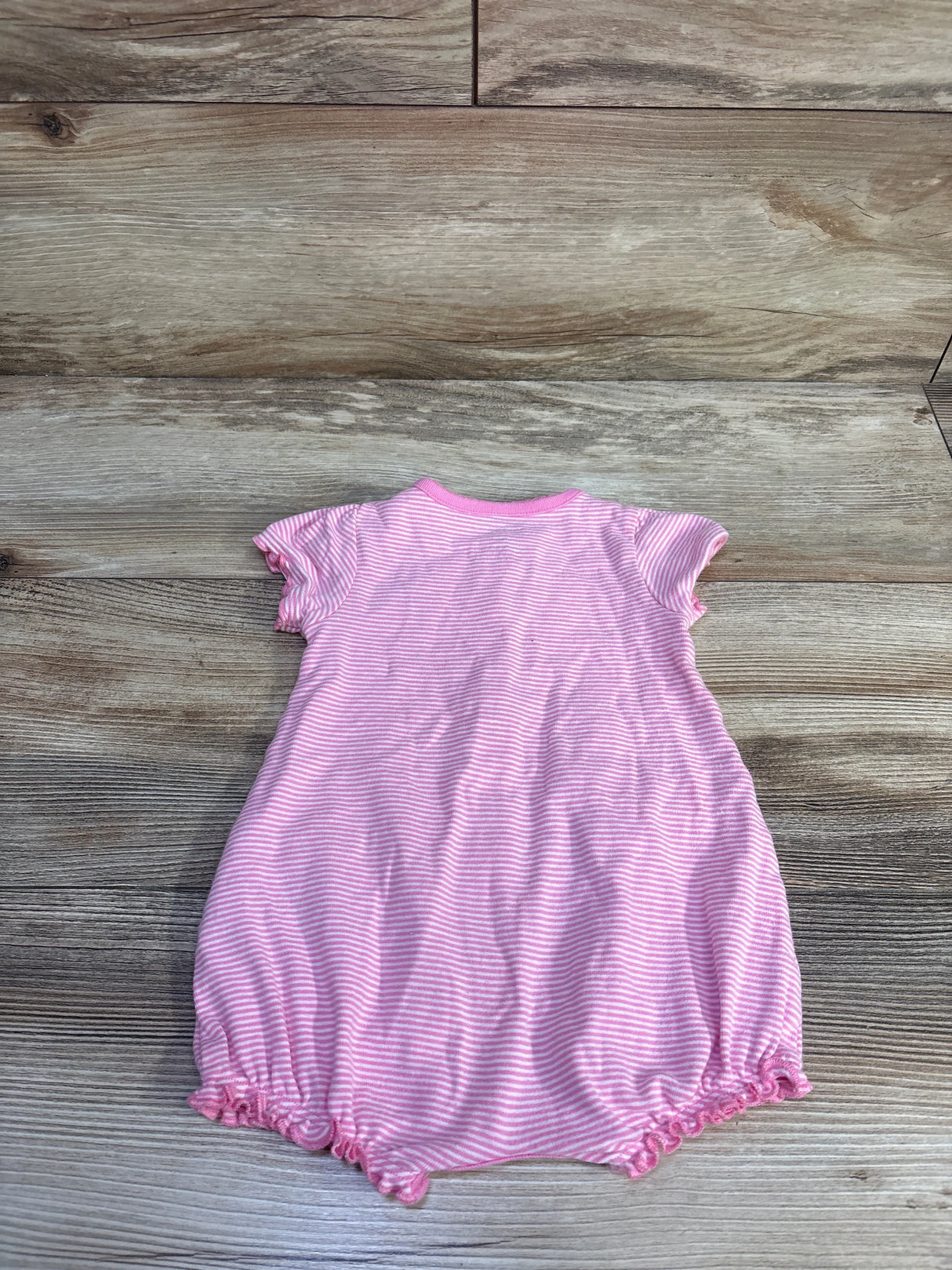 Flat-lay back view of pink-and-white striped shortie romper with short sleeves and ruffled elastic leg openings on wood backdrop