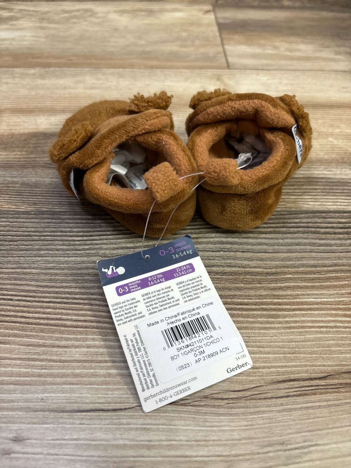 Top view of brown Gerber fleece lined non skid soft slipper booties showcasing soft cuffs on a wood grain background