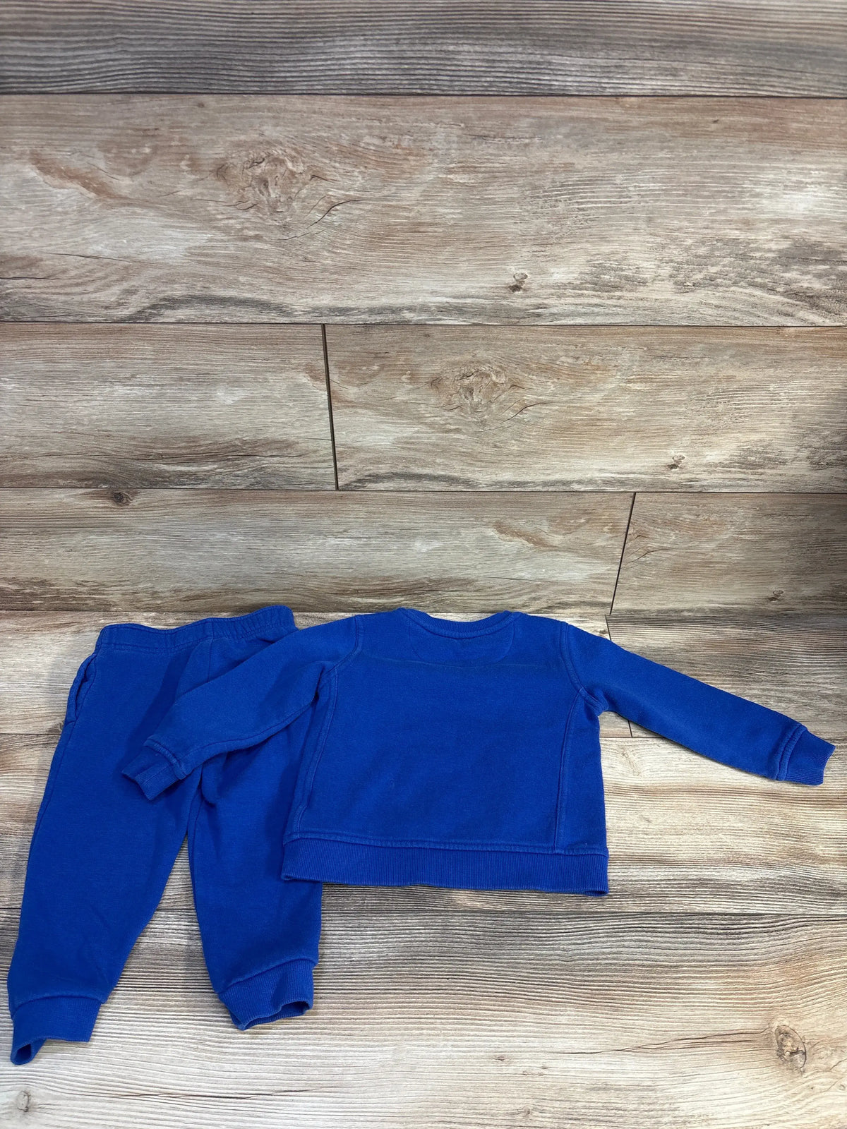 Flat lay of Reebok toddler pullover and joggers set showing crewneck top and elastic-waist joggers in royal blue on wood background