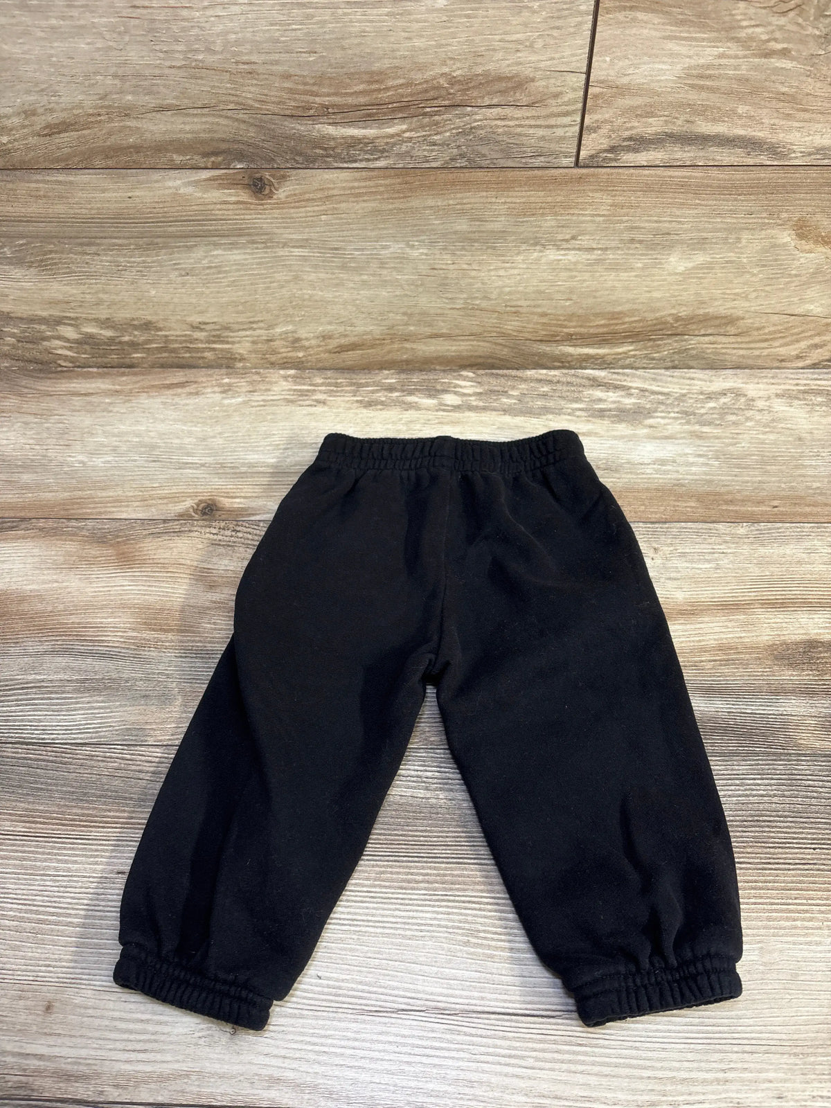 Flat lay of Baby Gap pull-on joggers size 12-18 months showcasing elastic waistband and gathered cuffs on wood floor background