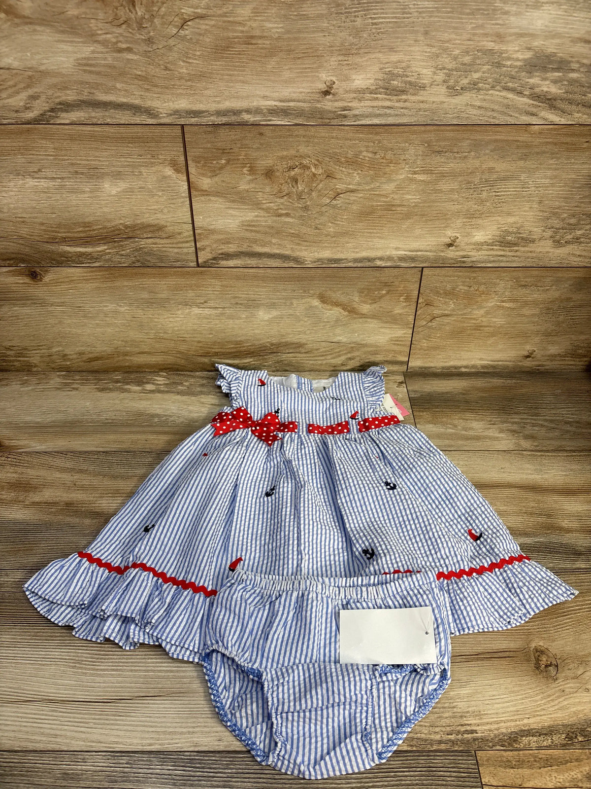 Front view of Rare Editions blue seersucker dress and bloomers showcasing embroidered details and red bow accents on wood floor