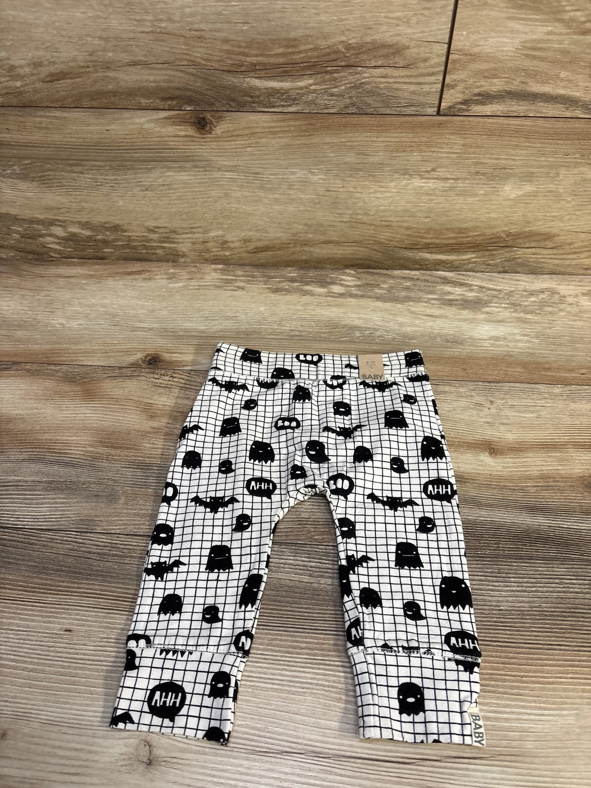 Flat lay of Cotton On baby Boo white leggings showing black ghost and bat print with ‘AHH’ speech bubbles and cuffed ankles on wood floor