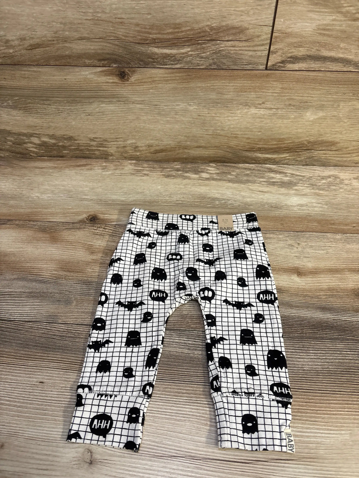 Flat lay of Cotton On baby Boo white leggings showing black ghost and bat print with ‘AHH’ speech bubbles and cuffed ankles on wood floor