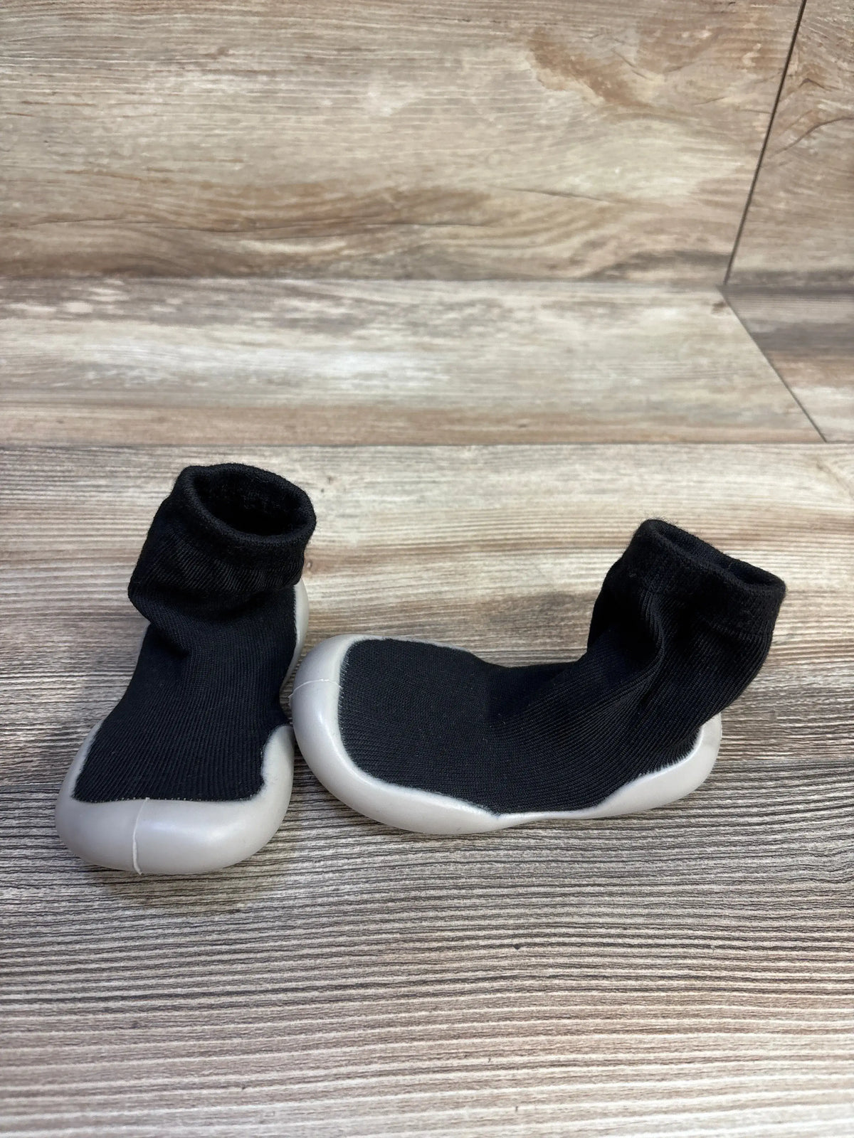 Front and side views of black baby sock shoes showcasing soft rubber soles on a wood-look background