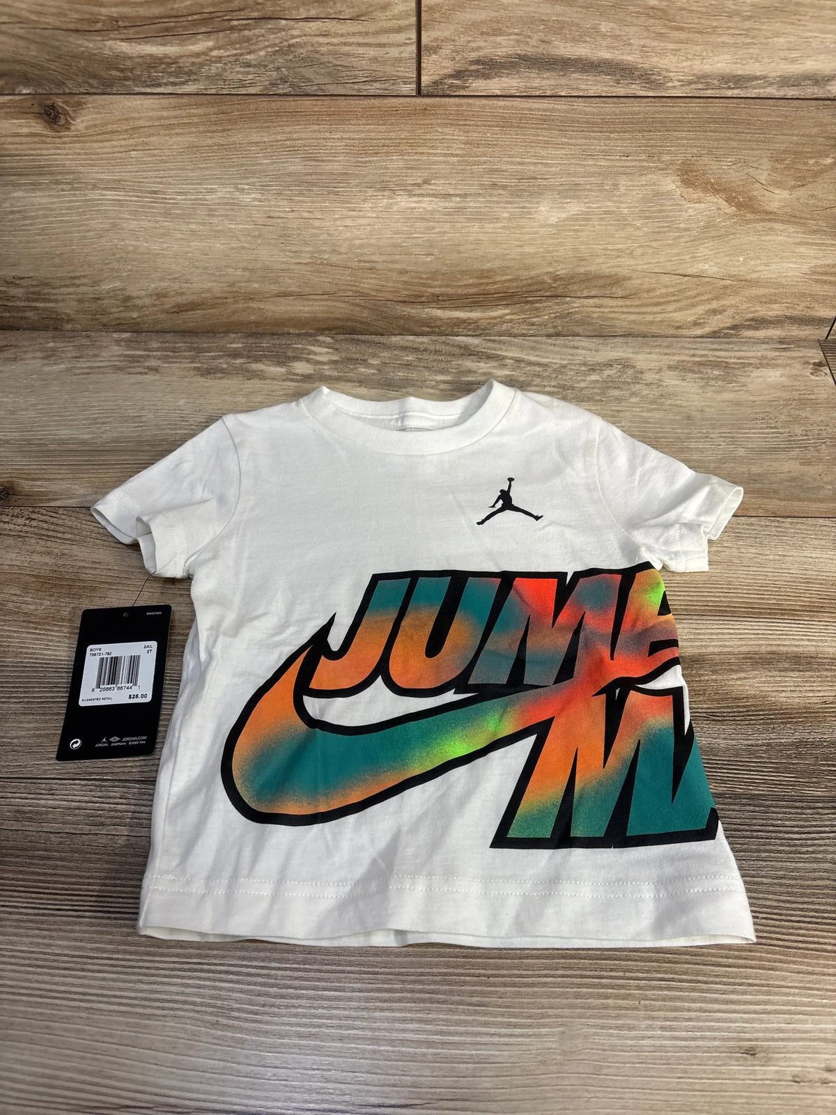 Front view of white Jordan Jumpman toddler shirt showcasing colorful oversized Jumpman graphic on a wood background