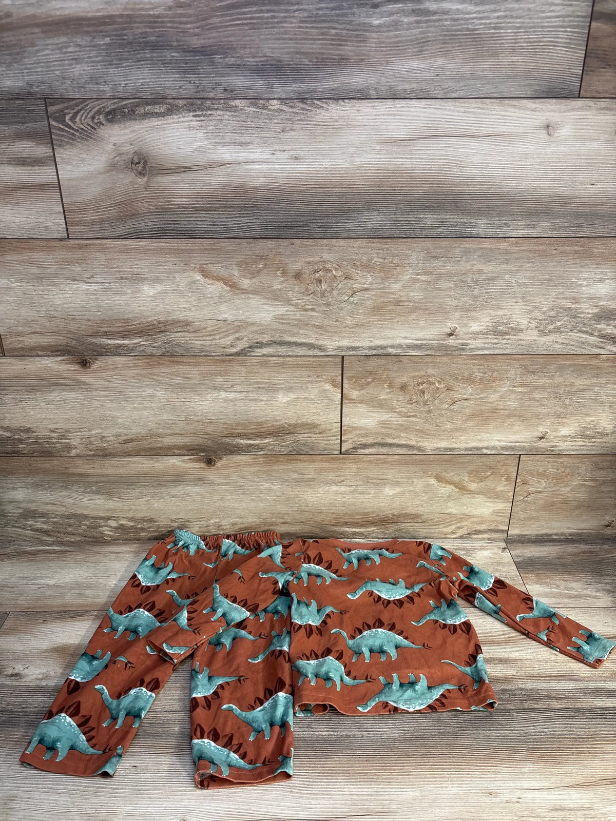 Flat lay of brown Just One You dinosaur henley pajama set showcasing dinosaur print with coordinating top and pants on wood flooring