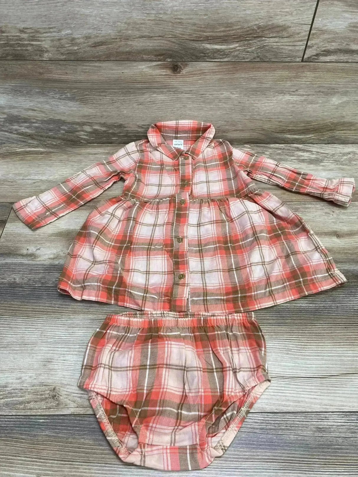 Flat lay of pink and brown plaid baby dress and matching bloomers showing button-front and gathered waist on wood background