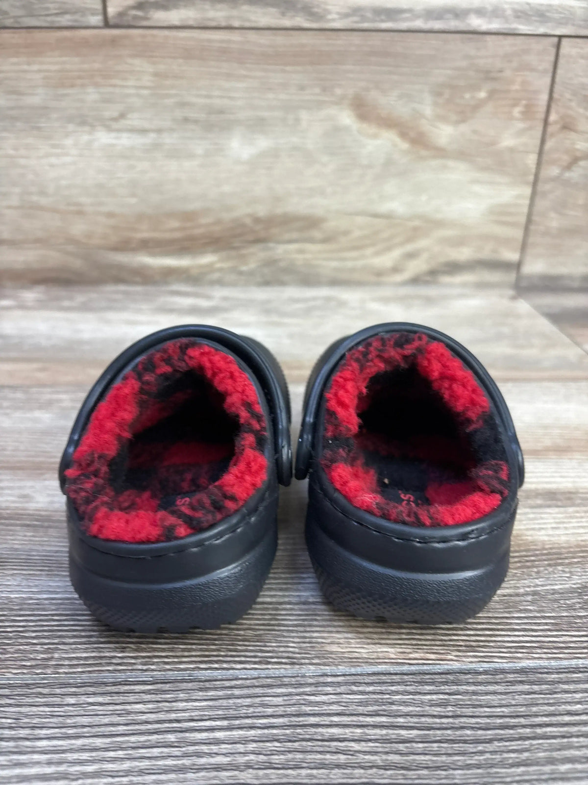 Rear view of Crocs Classic Lined Buffalo Check clogs (toddler 4C) showing red and black buffalo-check fleece lining on wood floor