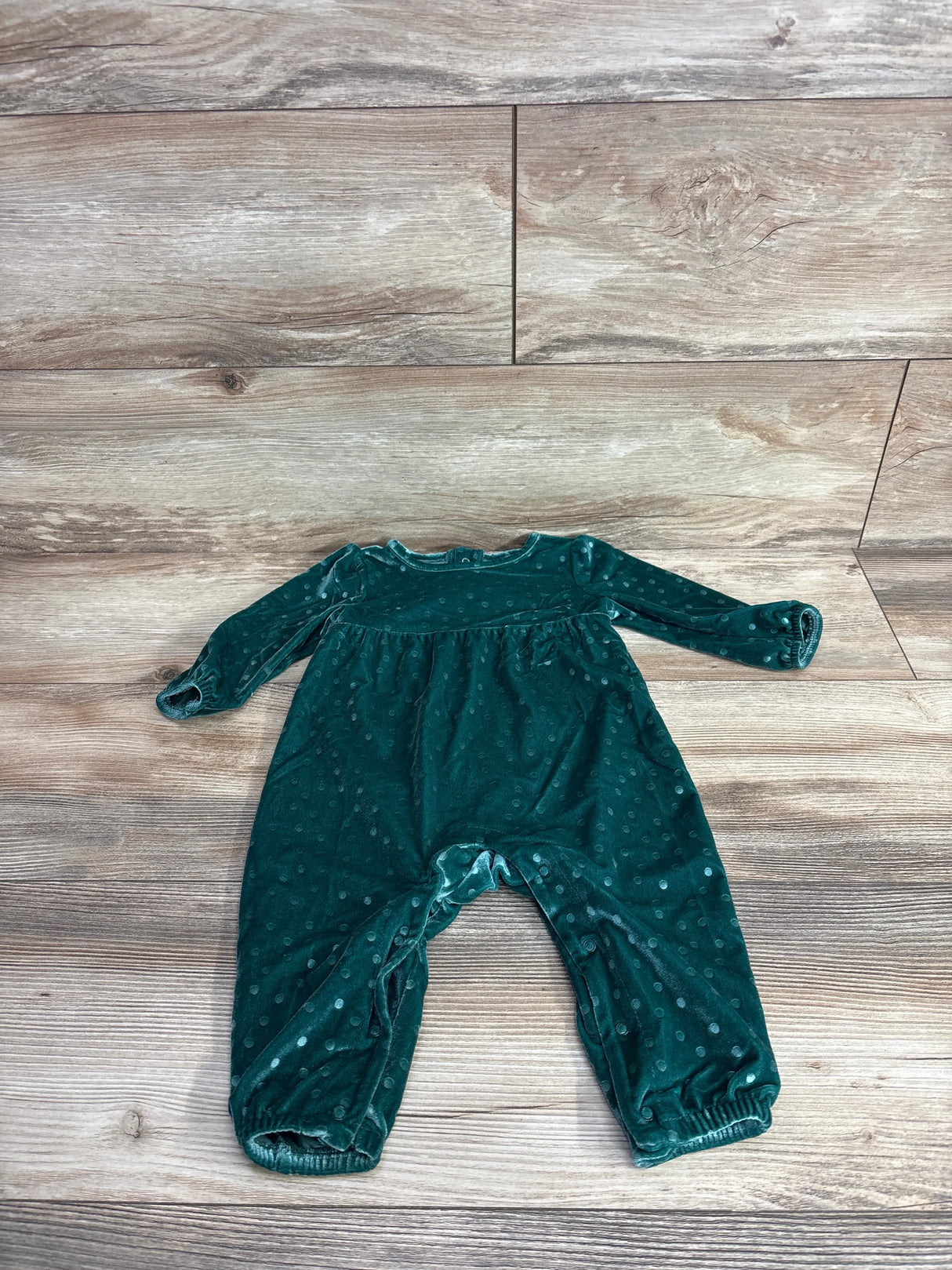 Green velvety baby romper with polka dot texture on wood background