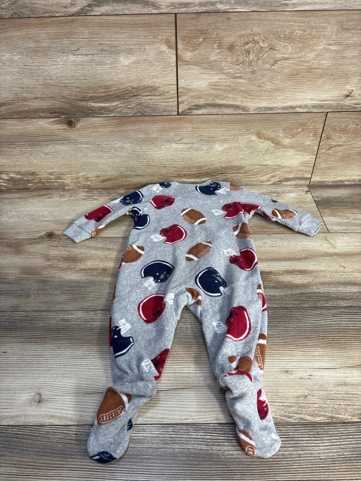 Front view of Carter’s grey football blanket sleeper showcasing football print and footed legs on a wood-look background