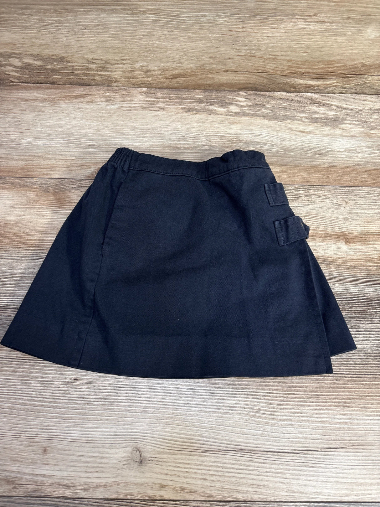 Flat lay of Dennis school uniform navy anchor skort size 4 showcasing pleated front with side buckle straps on wood plank floor