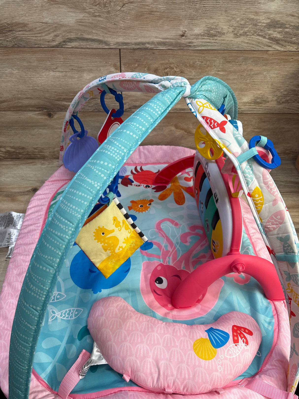 Angled view of Baby Einstein 4-in-1 Jellyfish Jamboree activity gym showcasing ocean play mat, arched toy bars with hanging toys and detachable piano on wood background