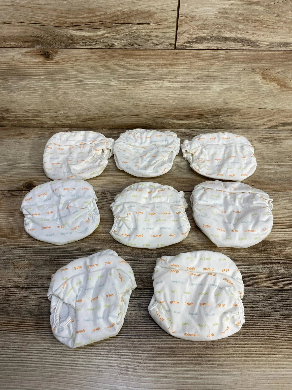 Overhead view of gDiapers newborn cloth diaper covers in ivory with small word print and elastic edges on wood background