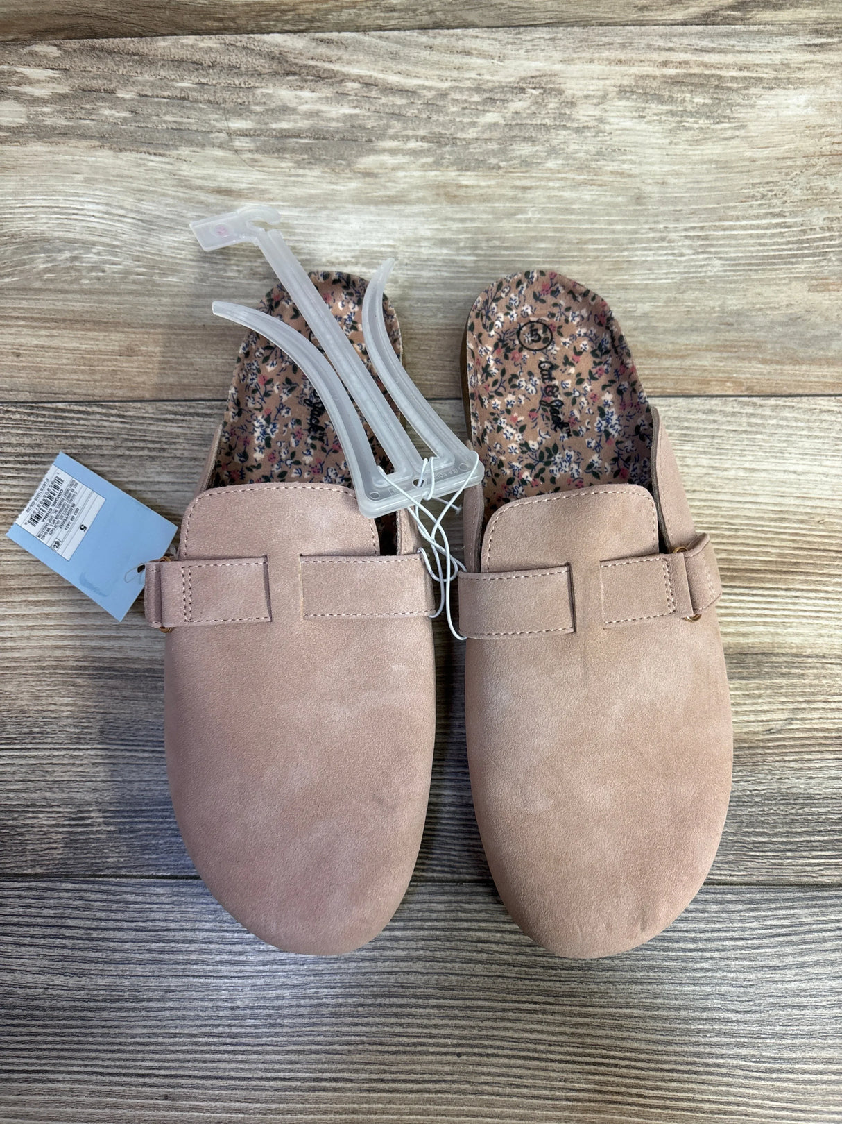 Pair of light pink suede slip-on women's shoes with floral insole on wooden floor