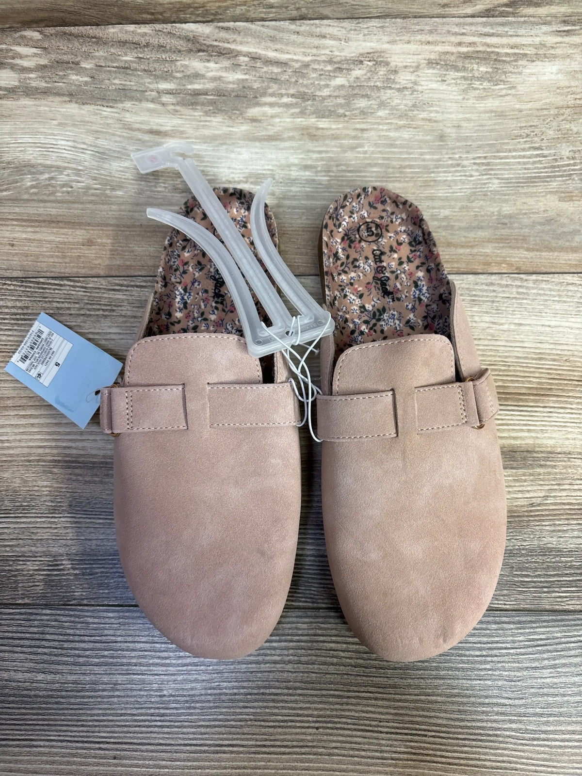Top view of NEW Cat & Jack Perry Clogs sz 5Y in blush suede with strap detail floral patterned footbed and attached hangtag on wood plank floor