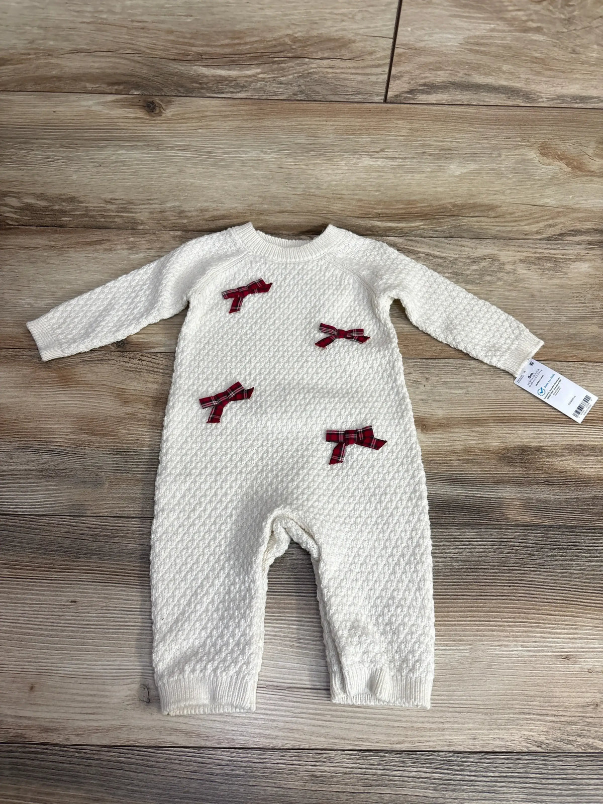 White knit baby onesie with red plaid bows, 6 months, laid on wood floor