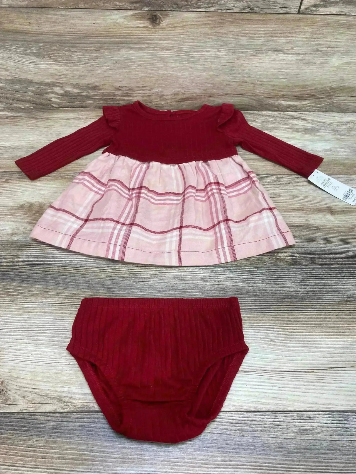 Flat lay of baby red ribbed long-sleeve dress with pink plaid skirt and matching red ribbed bloomers, size 6M, on light wood background