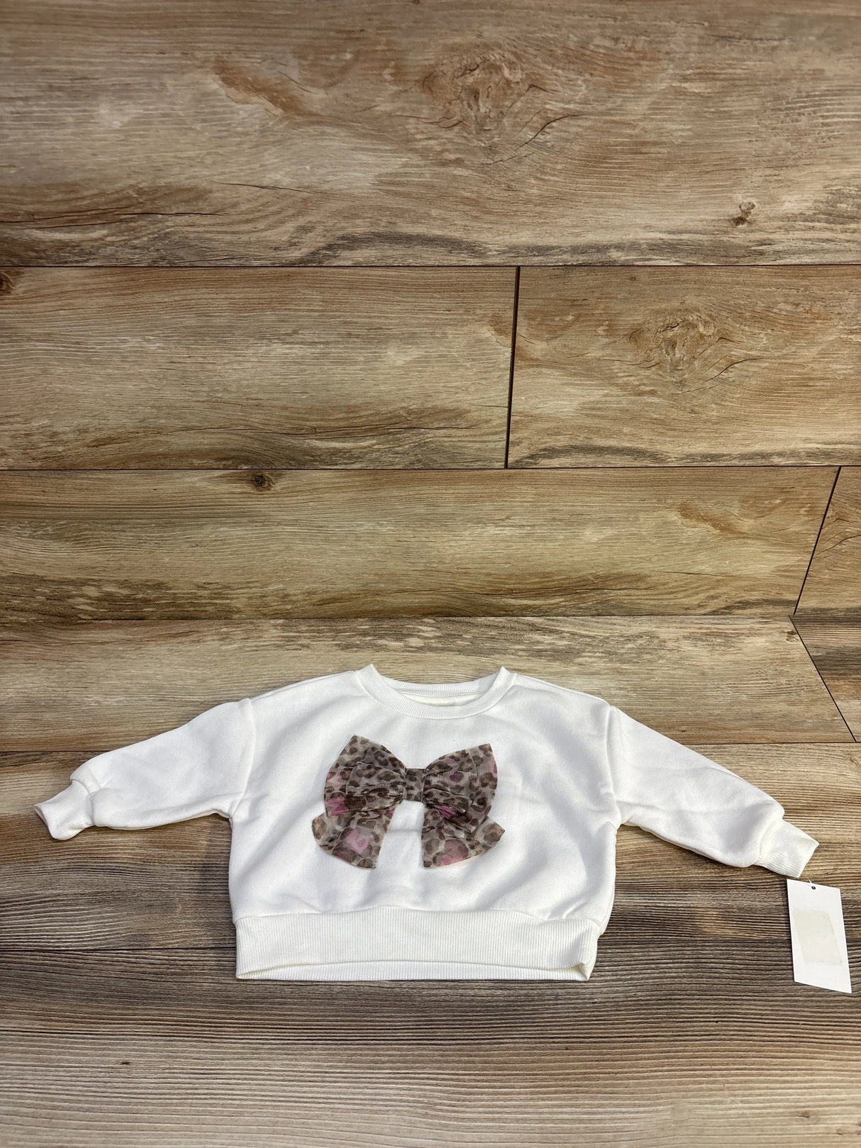 Front view of Disney Junior Minnie Mouse white baby sweatshirt size 12 months with large leopard print bow on wood floor