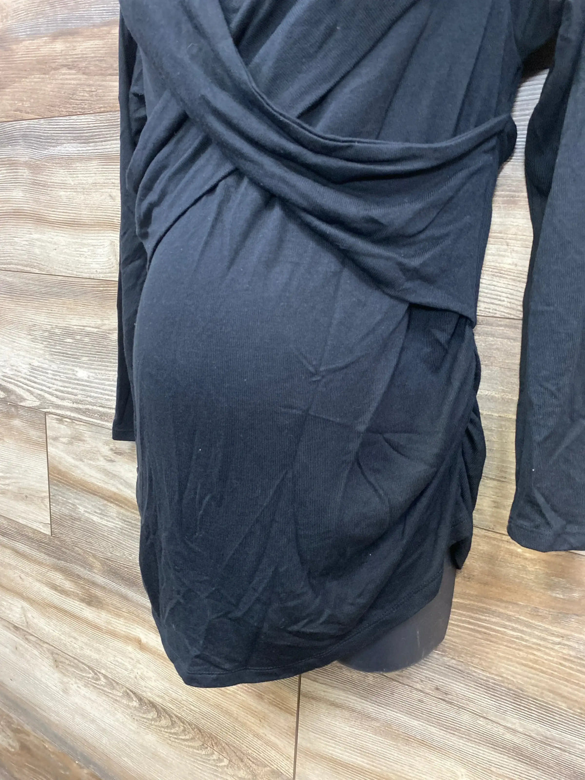 Black maternity top with ruched sides displayed on mannequin against wood background