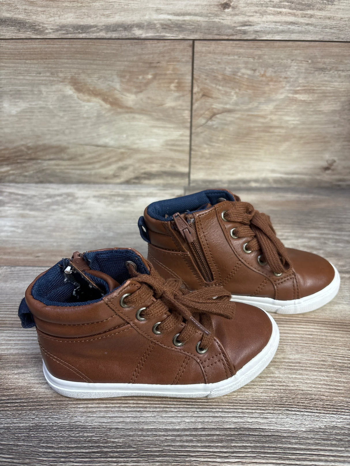 Angled view of brown Cat and Jack toddler high-top sneakers with side zipper and white sole on wood background