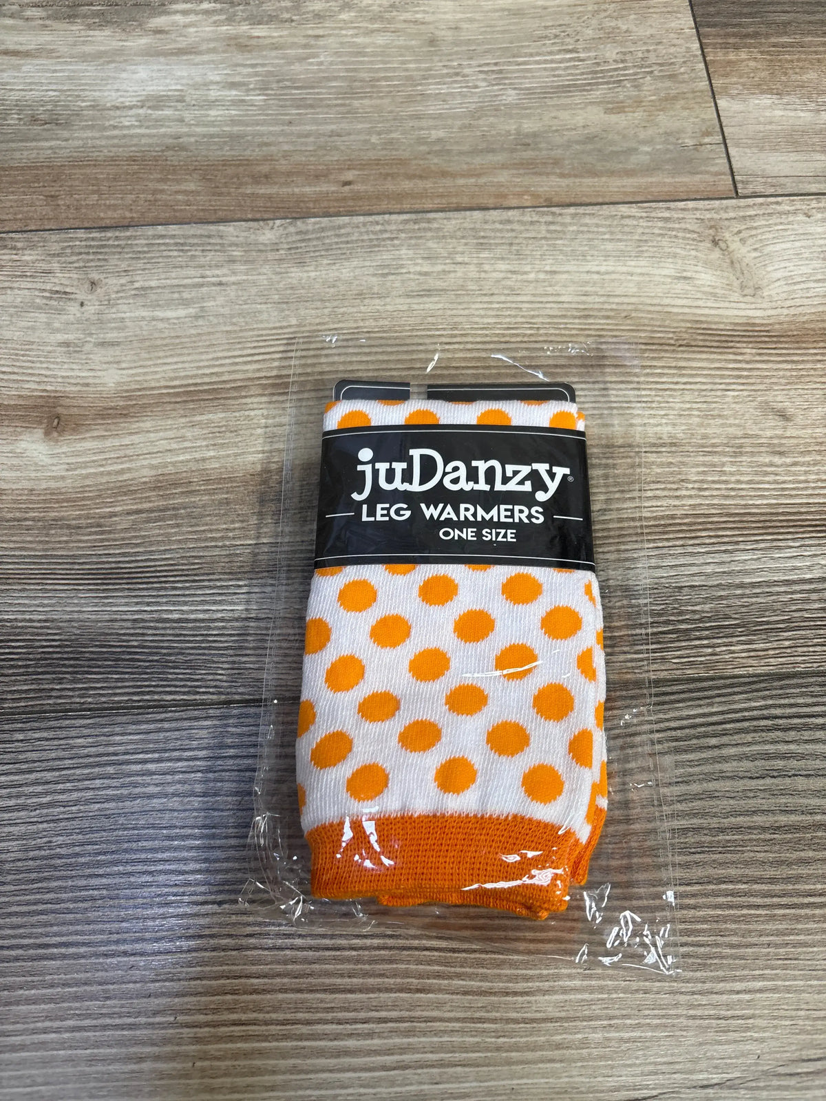 Front view of JuDanzy Halloween polka dot leg warmers showing orange and white dots and orange cuffs on wood grain