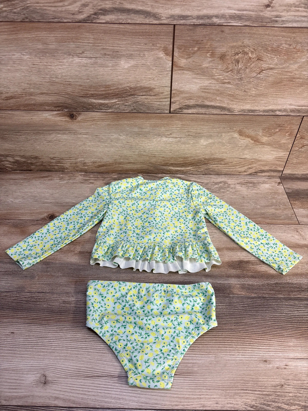 Flat-lay of 2-piece lemon-print rash guard with ruffle hem and matching high-waist bikini bottoms size 2T on wood background