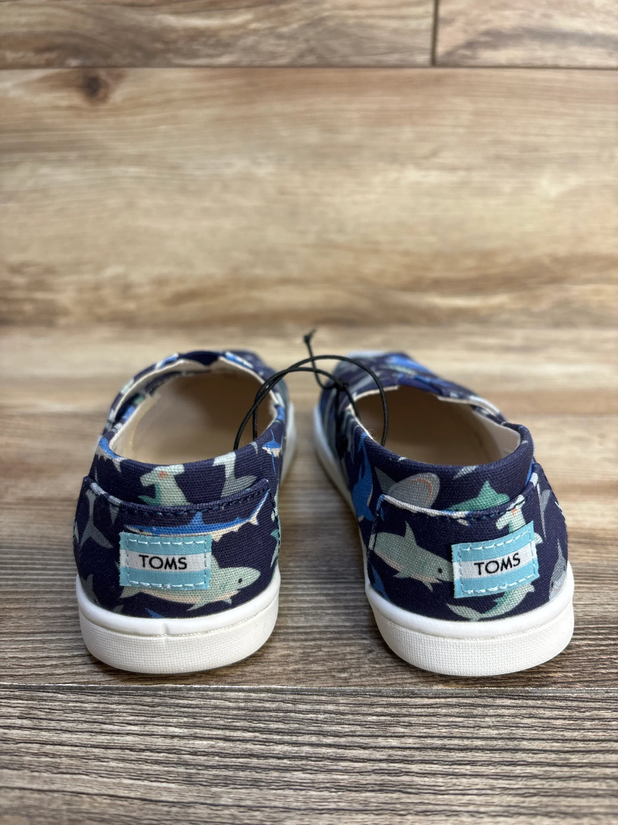 TOMS baby shoes with shark print, navy blue canvas, white sole, kids footwear on wood floor