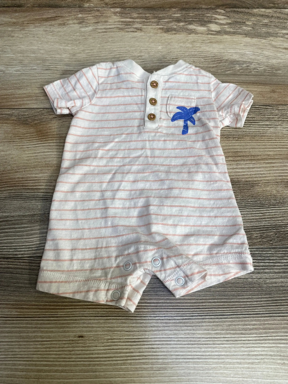 Flat lay of newborn white striped henley romper with button placket, blue palm tree on chest pocket and leg snaps on wood