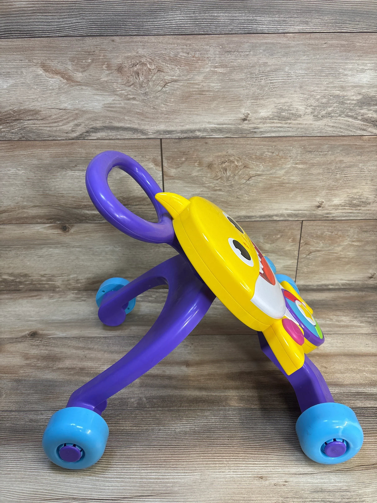Colorful baby walker with purple handle, yellow shark design, and blue wheels on wooden floor