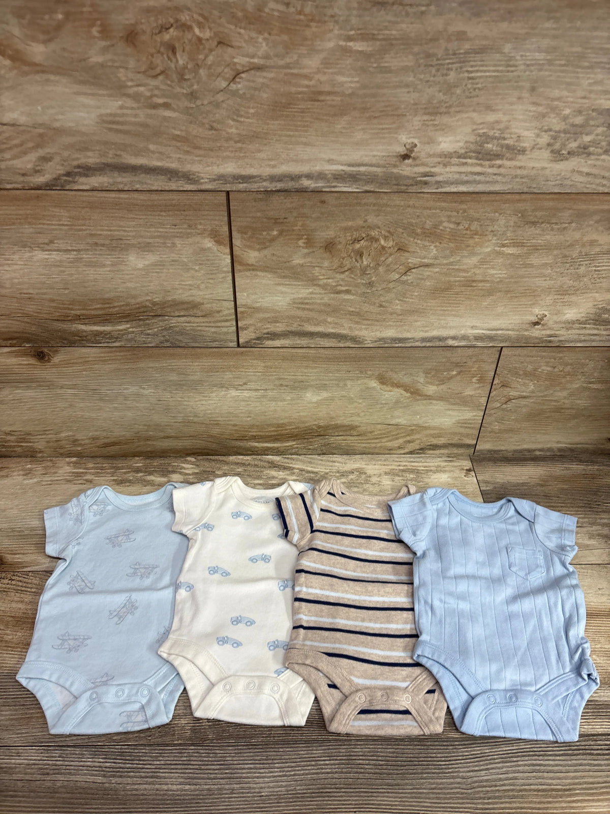 Top view of Member’s Mark four-pack organic newborn bodysuits in blue, cream, and striped designs on a wood floor