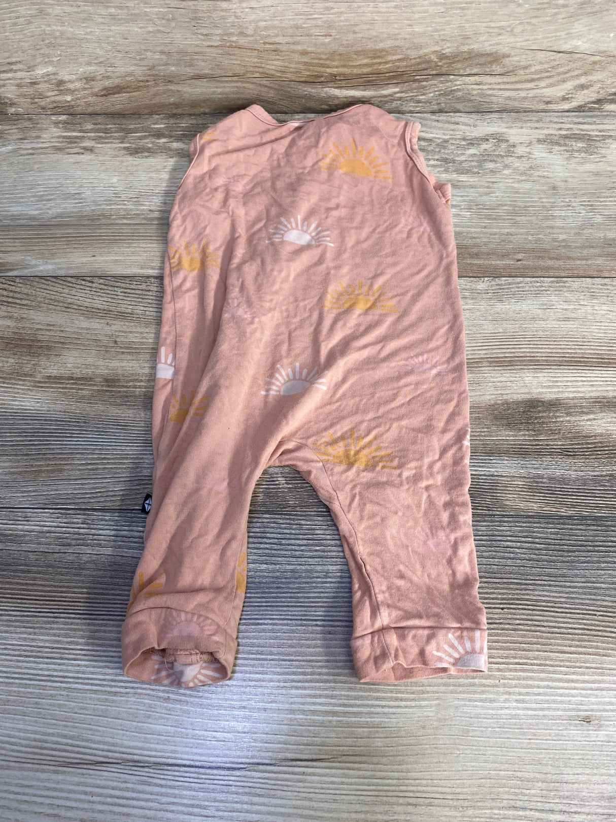 Flat lay of Kyte Baby sleeveless bamboo zip romper in peach showing front zipper and sunrise print on light wood background