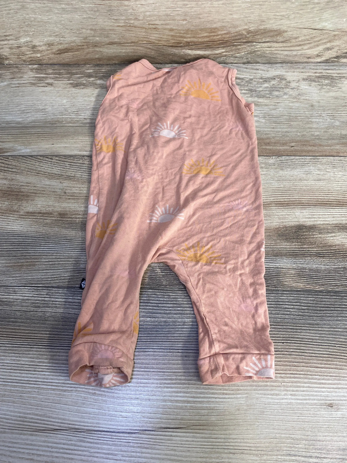 Flat lay of Kyte Baby sleeveless bamboo zip romper in peach showing front zipper and sunrise print on light wood background